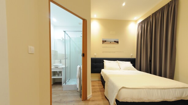 A bedroom with a bed, a bathroom with a glass shower, and a view of the beach. - Naya - Downtown Guesthouse (Porto)