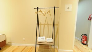 A room with a wooden floor, a bed, a black metal rack with hangers, and two towels labeled "NAYA". - Naya - Downtown Guesthouse (Porto)