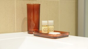 A bathroom with a white sink, a brown glass vase, and two bottles of lotion on a tray. - Naya - Downtown Guesthouse (Porto)