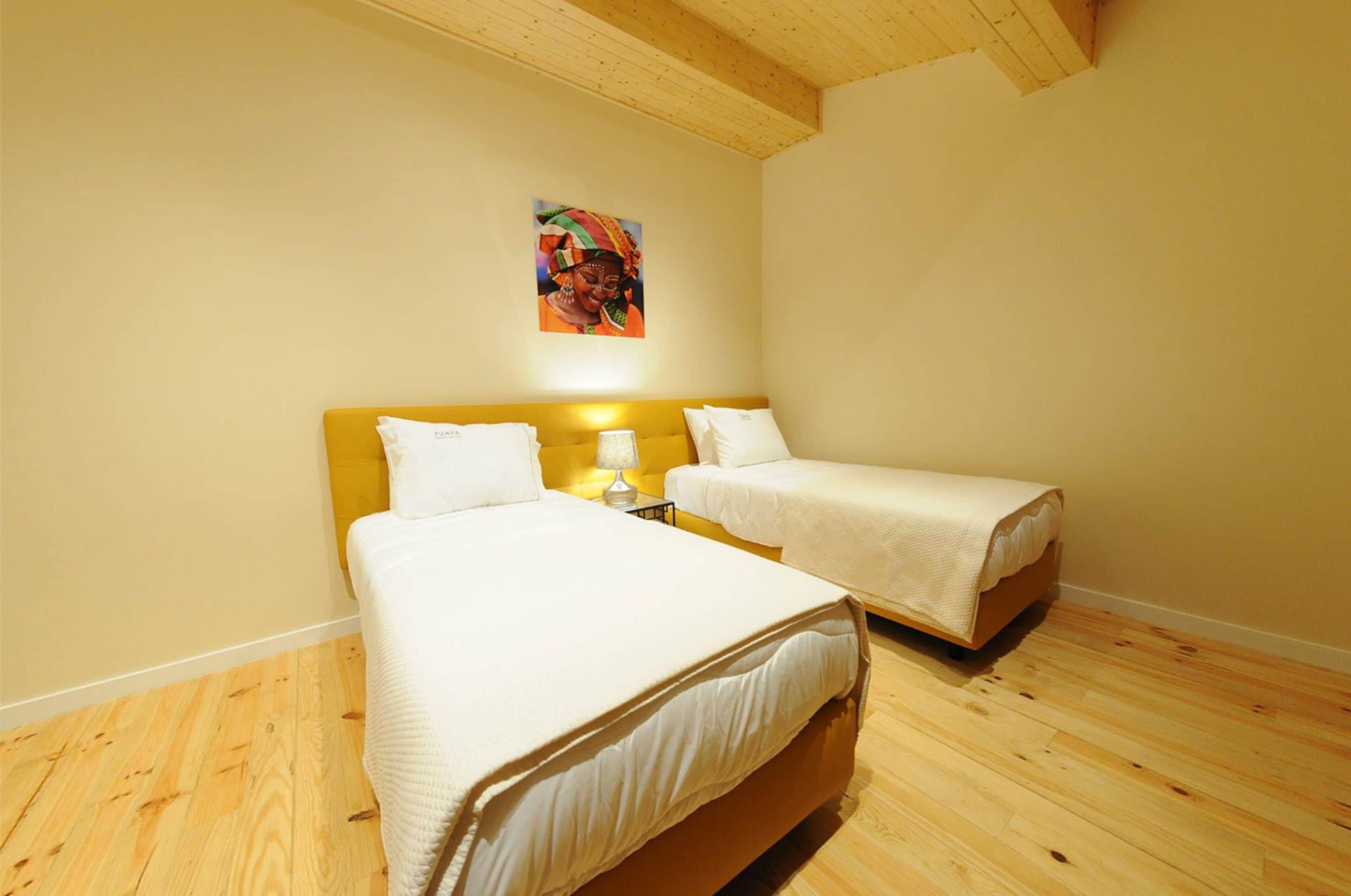 Una stanza con due letti, pavimento in legno e un quadro appeso al muro.