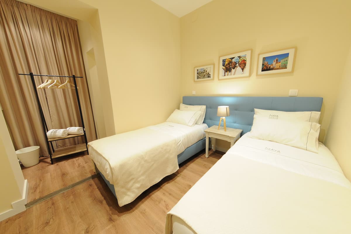 Habitació d'hotel amb dos llits, un armari, una taula de nit amb una làmpada i tres quadres al mur.