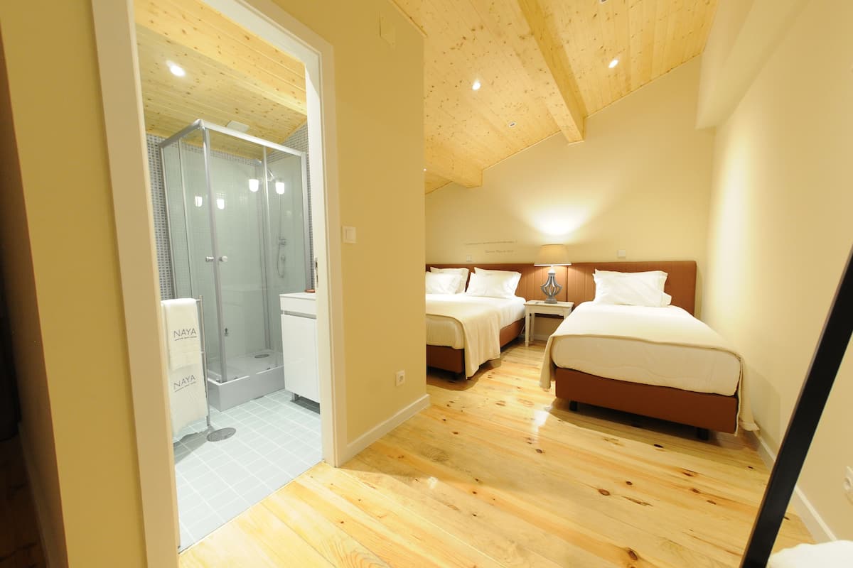 Un dormitori amb dos llits, sostre de fusta i una cabina de bany amb vidre.
