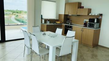 A modern kitchen with white cabinets, a dining table with four chairs, and a view of greenery outside.