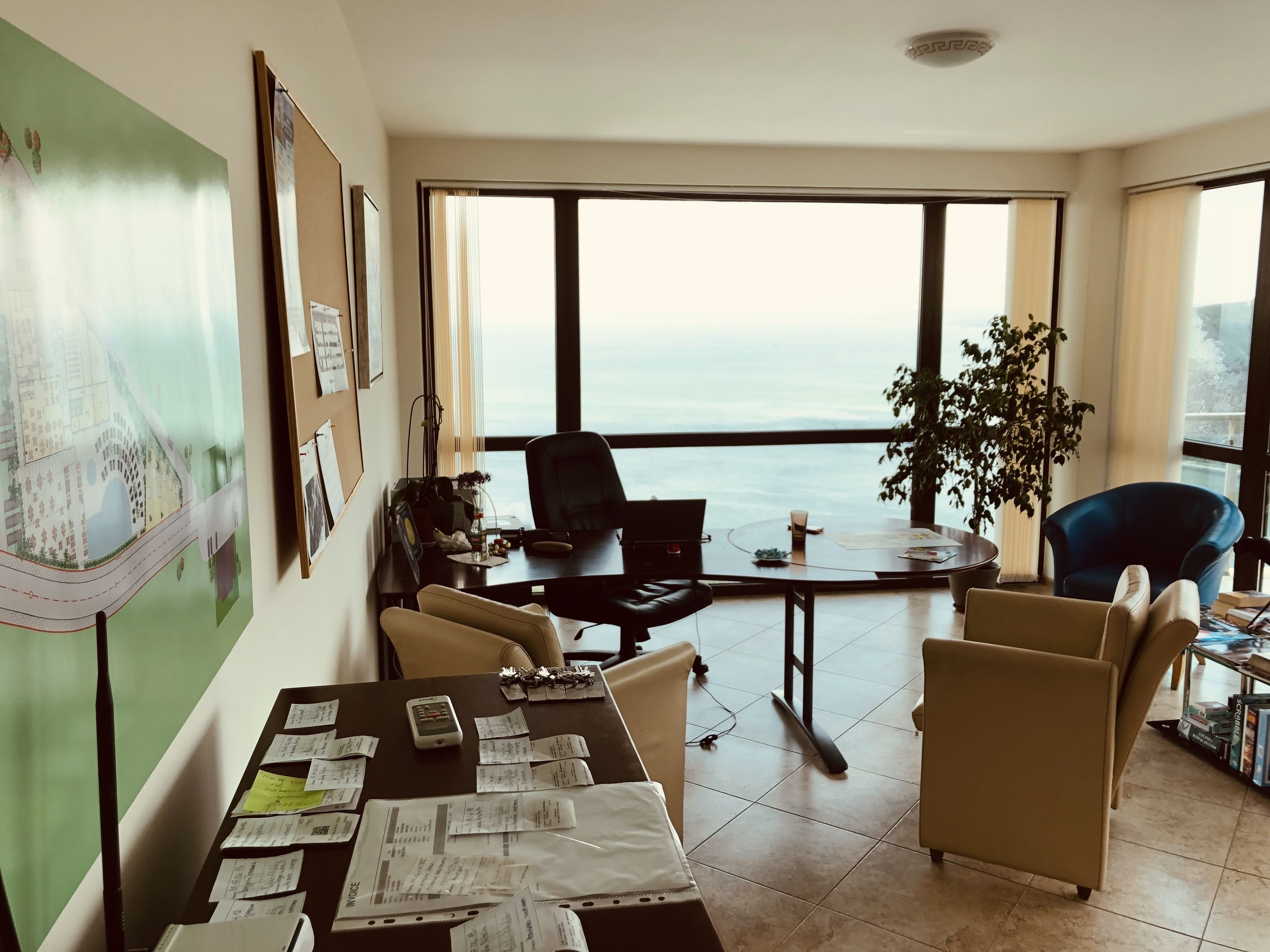 A spacious office with a large desk cluttered with papers, a laptop, and a plant.