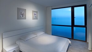 Une chambre avec un grand lit, une table de chevet et une vue sur la mer, accessible par une porte-fenêtre coulissante.