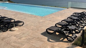 Un espace aménagé au bord de la piscine, avec des chaises longues et une vue sur l’océan.