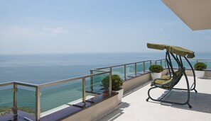 Un balcón con una silla mecedora, plantas en macetas y vista al mar.