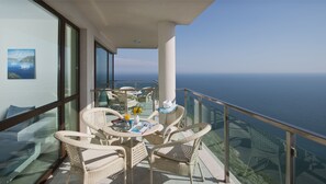 A balcony with wicker furniture, a glass table, and a view of the sea.