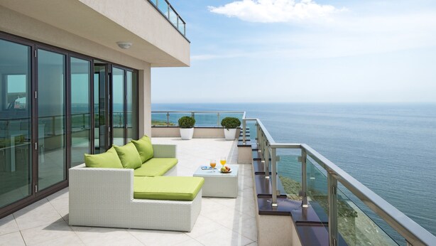 Un balcon moderne avec un canapé blanc, des coussins verts et une petite table sur laquelle sont disposés des fruits.