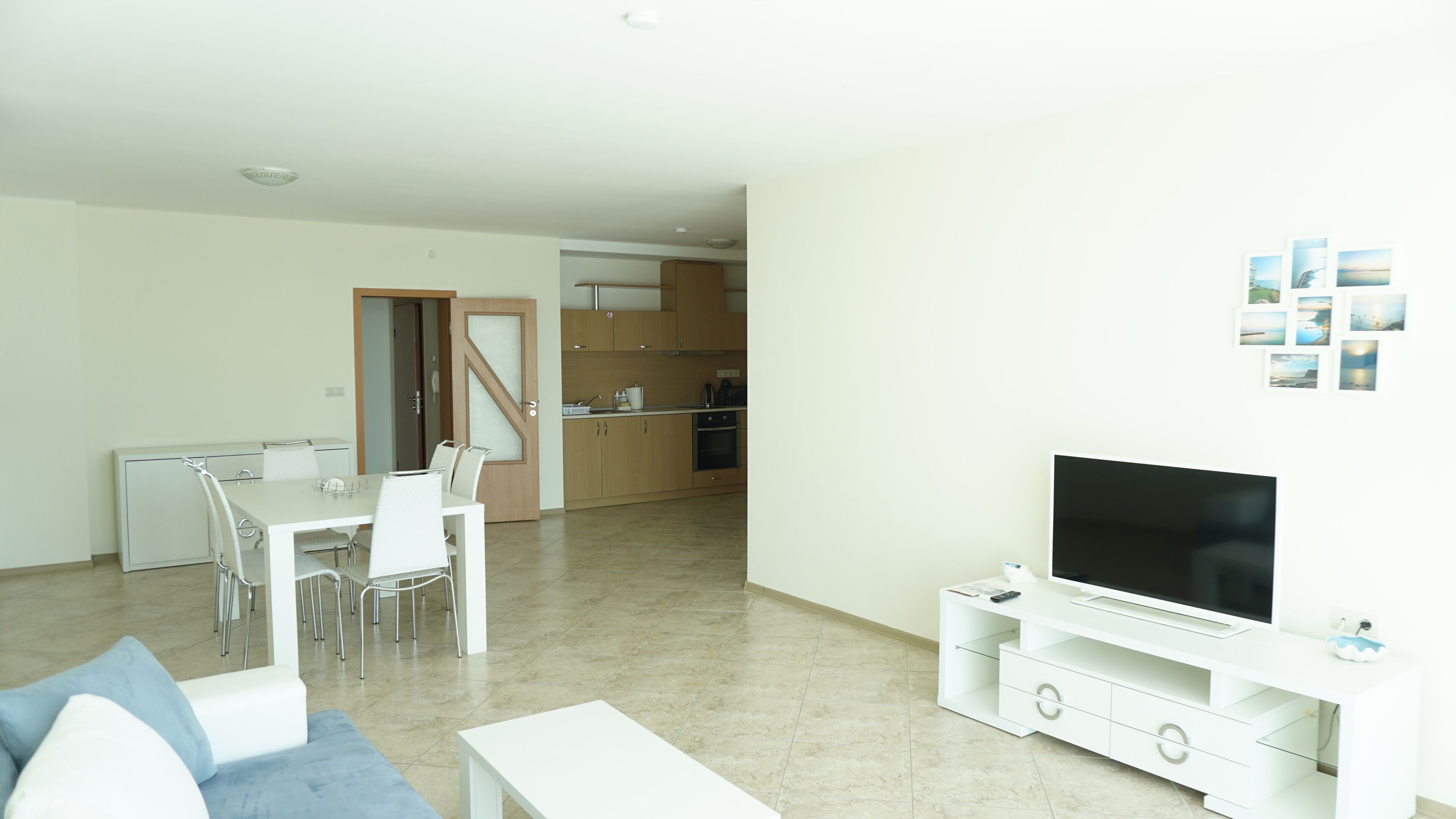 A modern living room with a TV, white furniture, and a dining area with chairs and a table.
