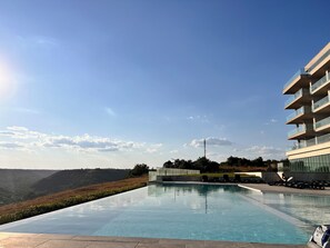 Un hotel moderno con piscina infinita en la azotea y vistas a un paisaje montañoso.