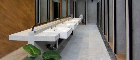 Un baño moderno con tres lavamanos, un espejo grande y una planta.