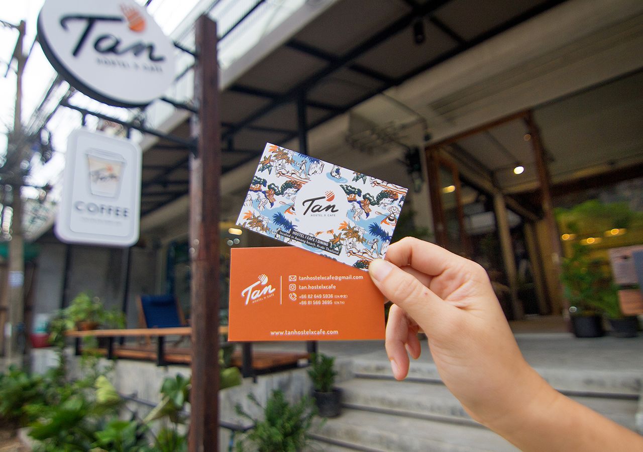 A hand holding a business card and a sign for Tan Hostel & Cafe.