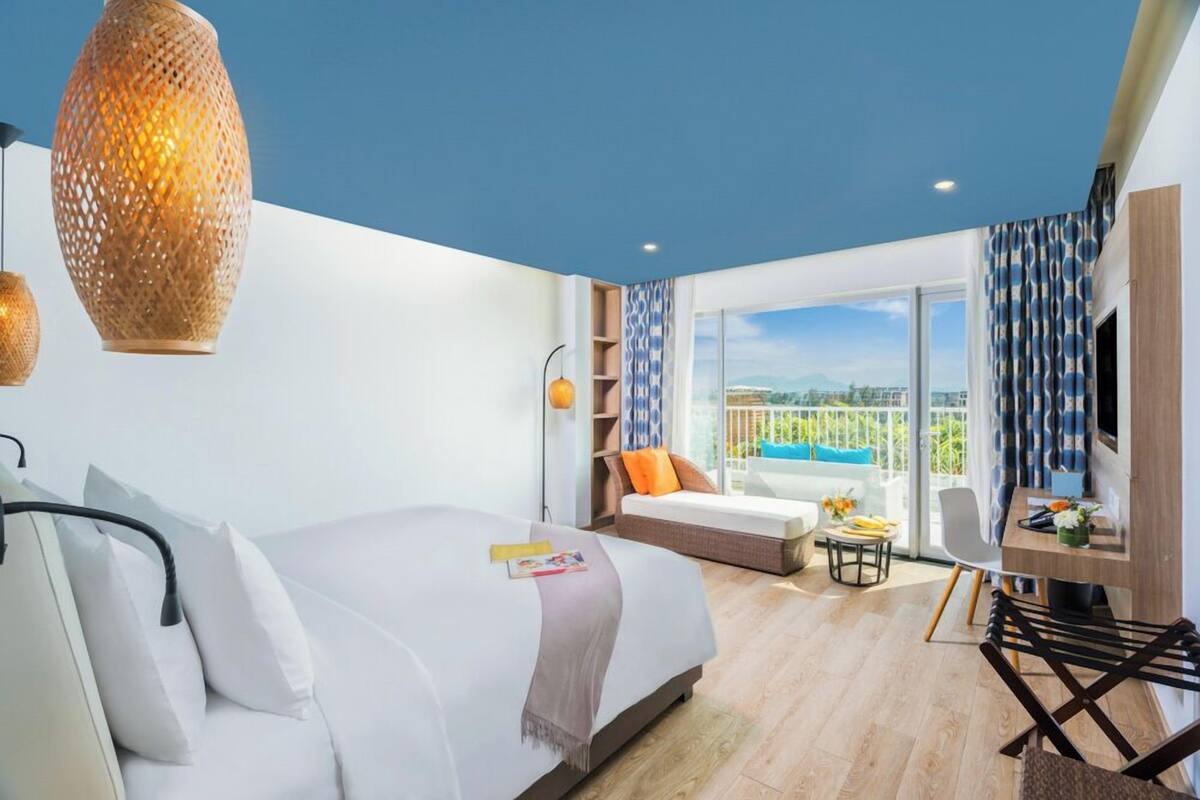 A modern hotel room with a bed, a desk, a sofa, and a balcony with a view.