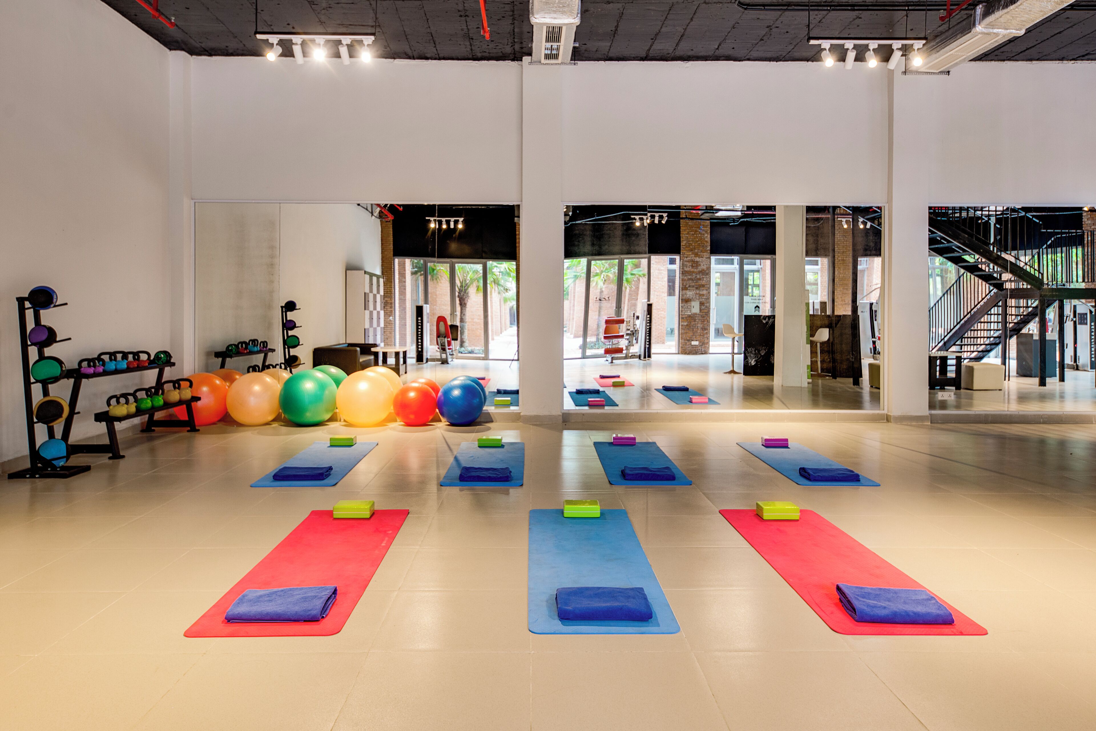 Une salle de sport intérieure spacieuse, équipée de différents tapis de sol, de ballons colorés et de matériel de musculation.