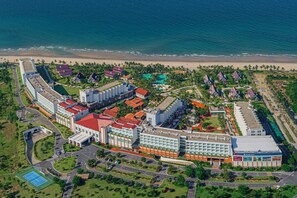 Vista aérea de un complejo turístico costero con varios edificios, una playa y una gran piscina.