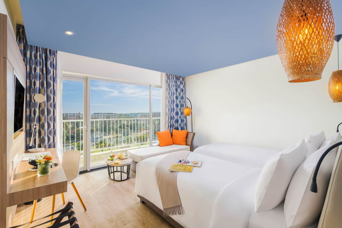 A hotel room with a balcony, a bed, a desk, and a view of the city.