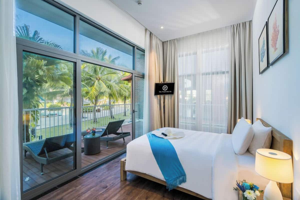 A hotel room with a large balcony, a bed with white bedding, a TV mounted on the wall, and a view of palm trees.