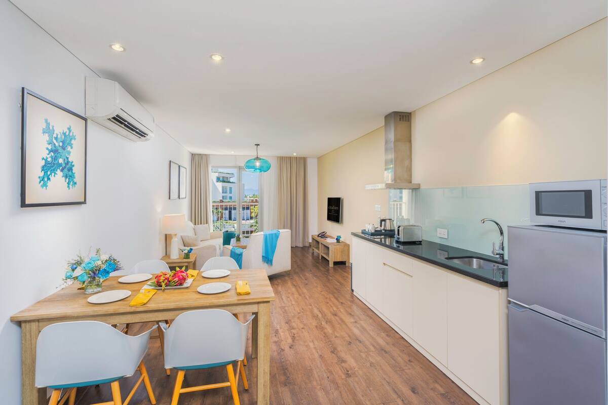 A modern kitchen with a dining area, featuring a wooden table, chairs, and a view of the city.