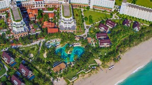 An aerial view of a resort with a large pool, beachfront, and multiple buildings. - The Pearl Hội An (Da Nang)