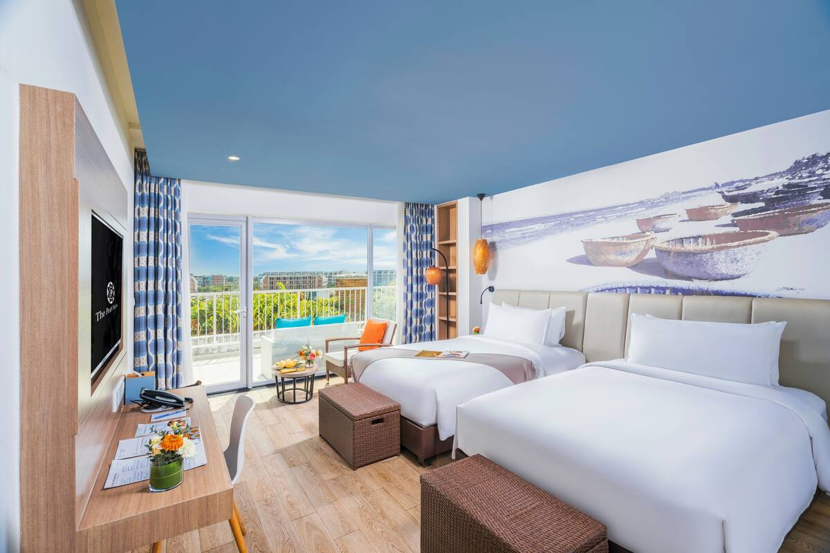 A hotel room with two beds, a desk, a TV, and a balcony with a view.