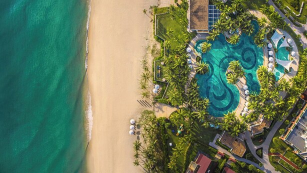 An aerial view of a resort with a large pool, palm trees, and a beach. - The Pearl Hội An (Da Nang)