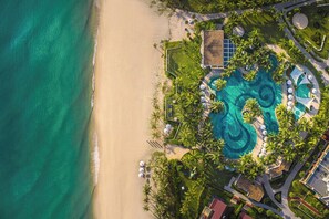 An aerial view of a resort with a large pool, palm trees, and a beach. - The Pearl Hội An (Da Nang)