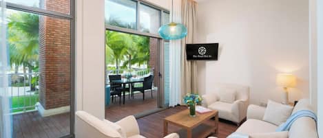 A hotel room with a large window, a wooden coffee table, two armchairs, a sofa, and a hanging pendant light.