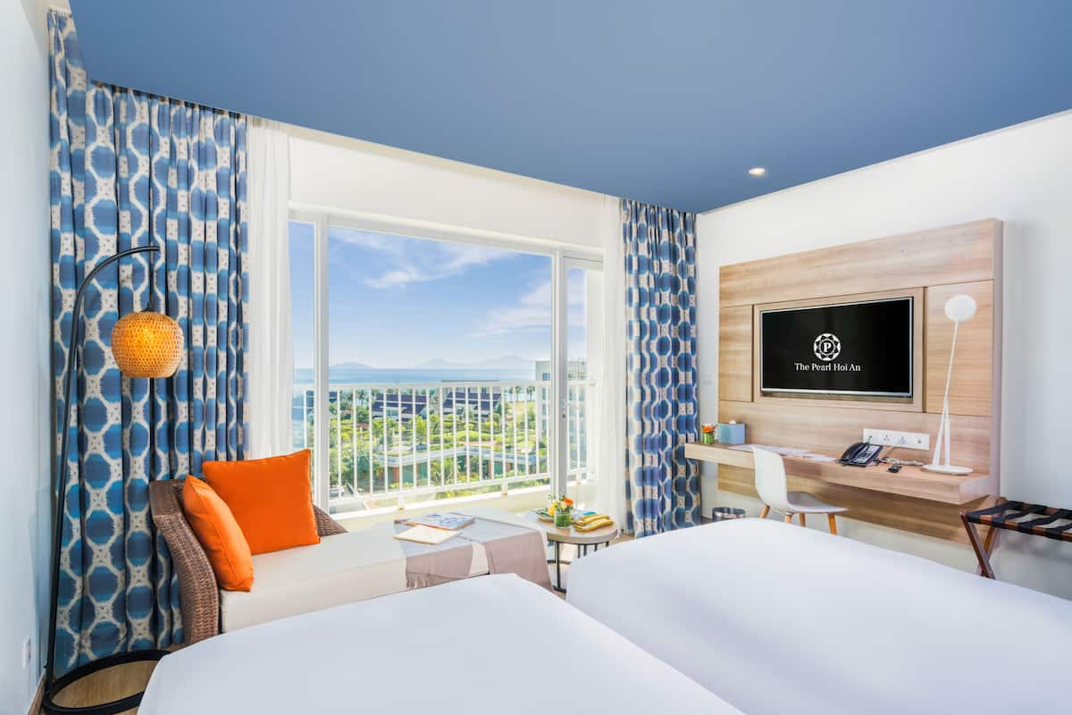 A hotel room with a bed, a desk, a TV, a balcony with a view, and patterned curtains.