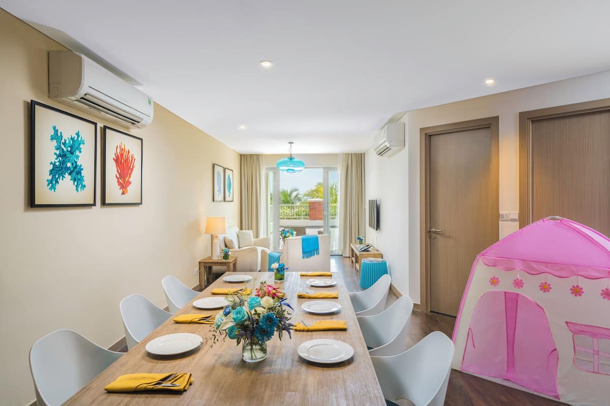 A dining room with a wooden table set for four, white chairs, a vase of flowers, and a pink play tent in the corner.