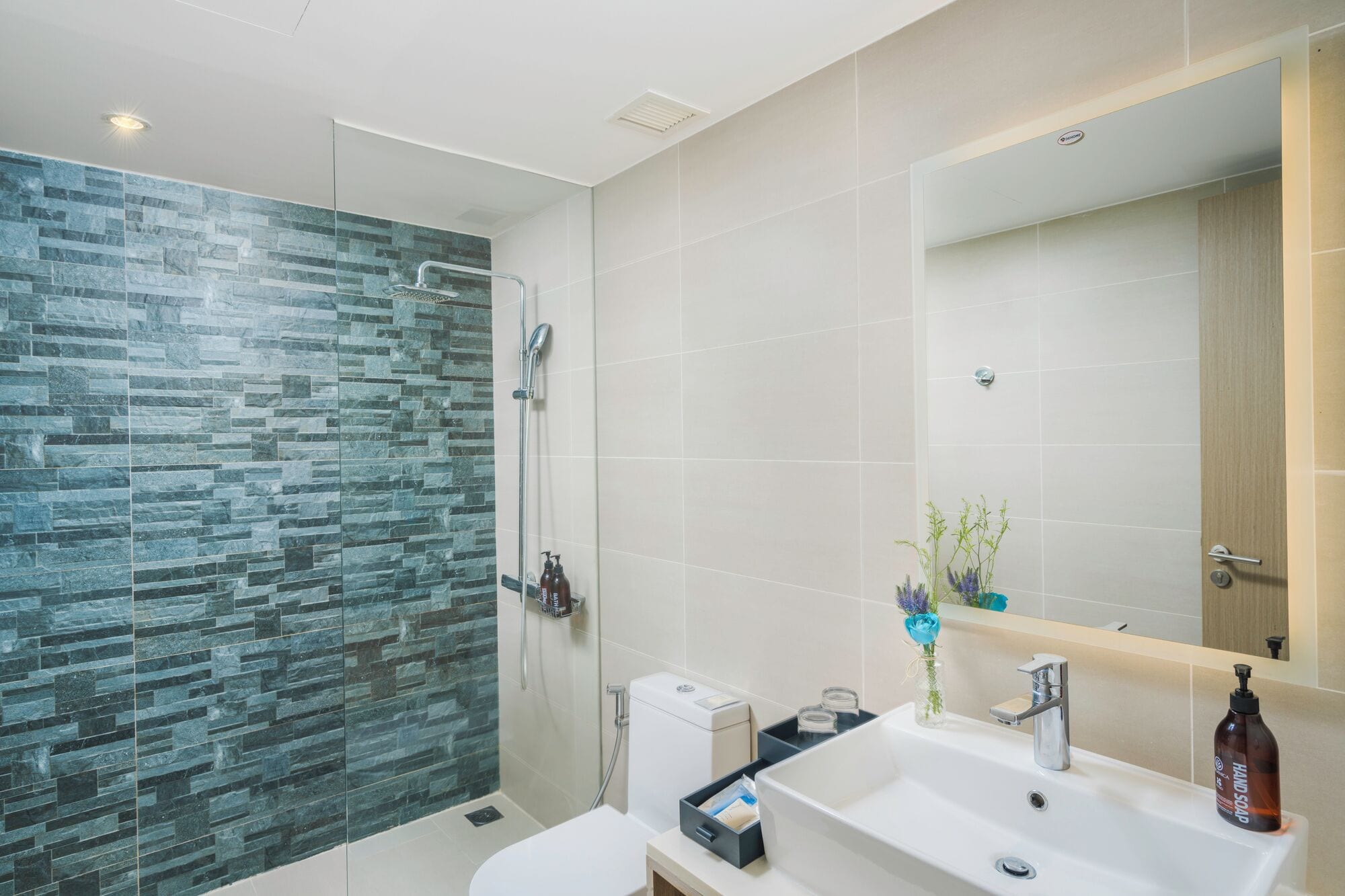 A modern bathroom with a glass shower enclosure, a white sink, and a mirror.