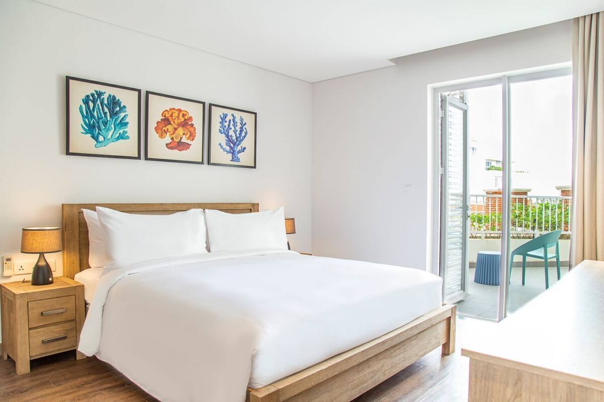 A hotel room with a large bed, a nightstand with a lamp, and a view of the outside balcony.