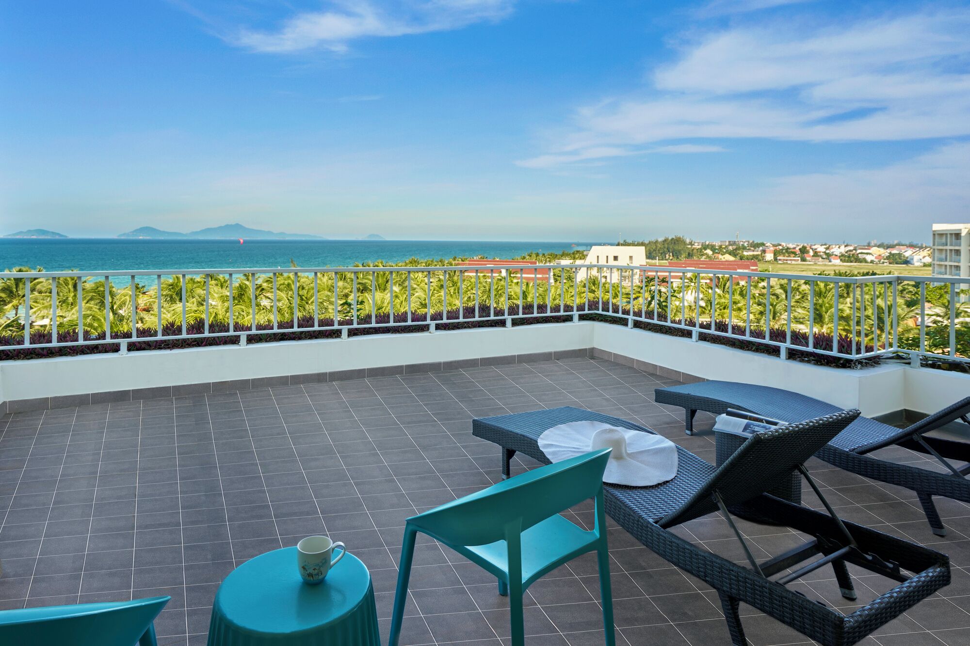 A terrace with a view of the sea, featuring a table, chairs, and a small table with a cup.