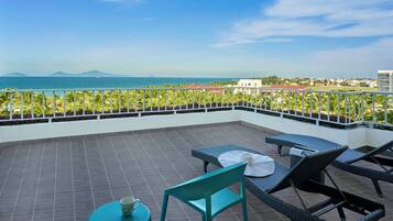 A terrace with a view of the sea, featuring a table, chairs, and a small table with a cup.