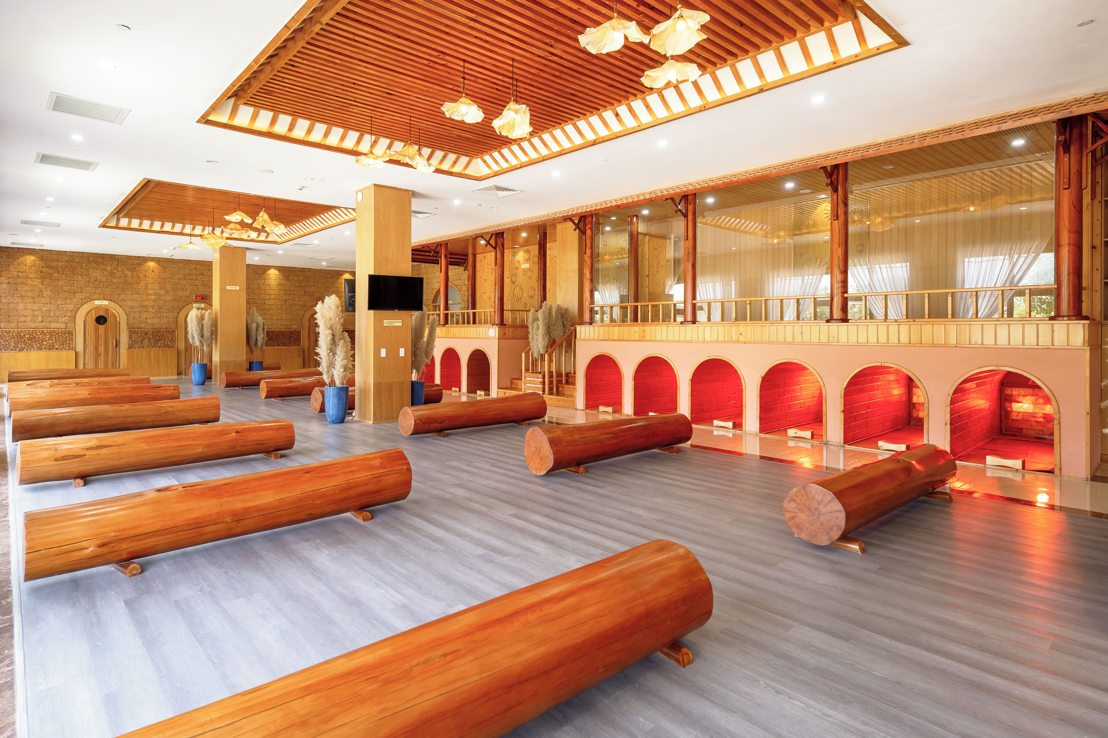 A spacious room with wooden logs as seating, large windows, and a high ceiling with wooden beams.