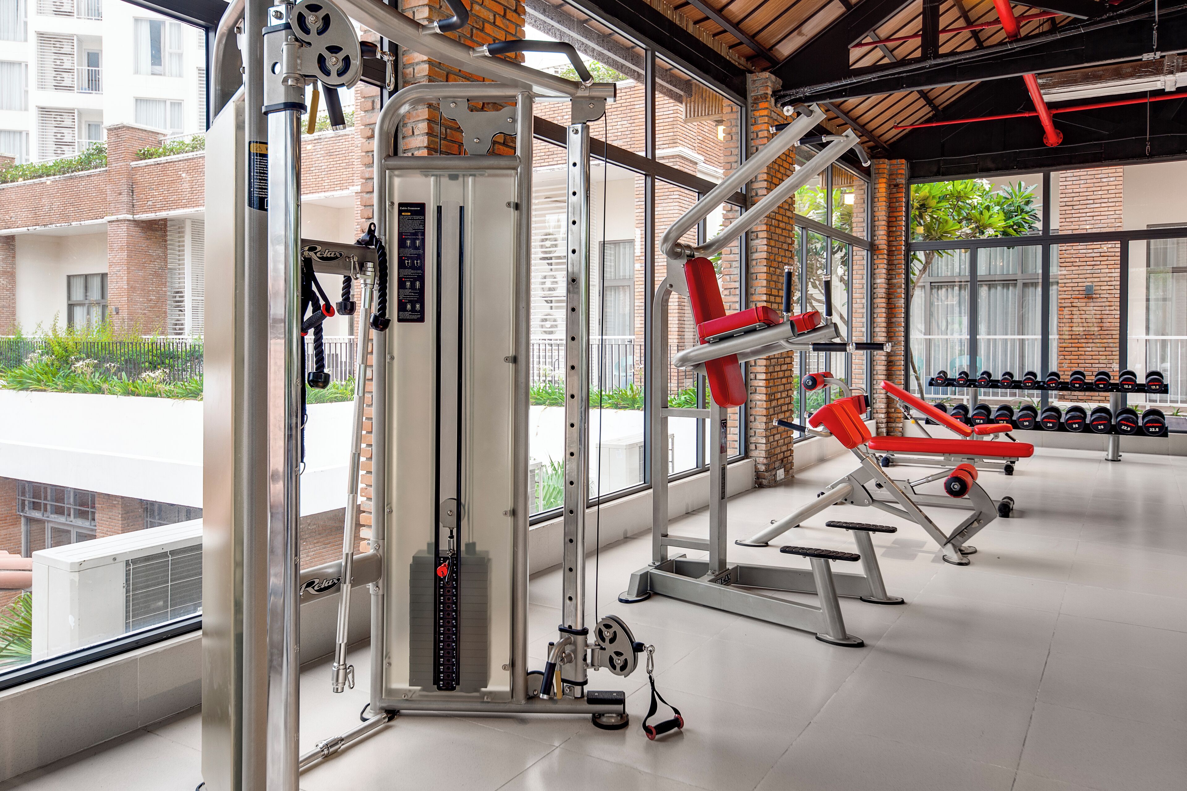 Une salle de sport équipée de divers appareils d’exercice, dotée de grandes fenêtres et offrant une vue sur les bâtiments environnants.