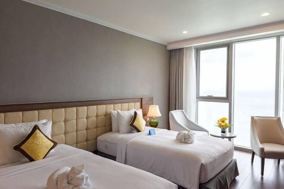 Een hotelkamer met twee bedden, een zithoek en een groot raam.