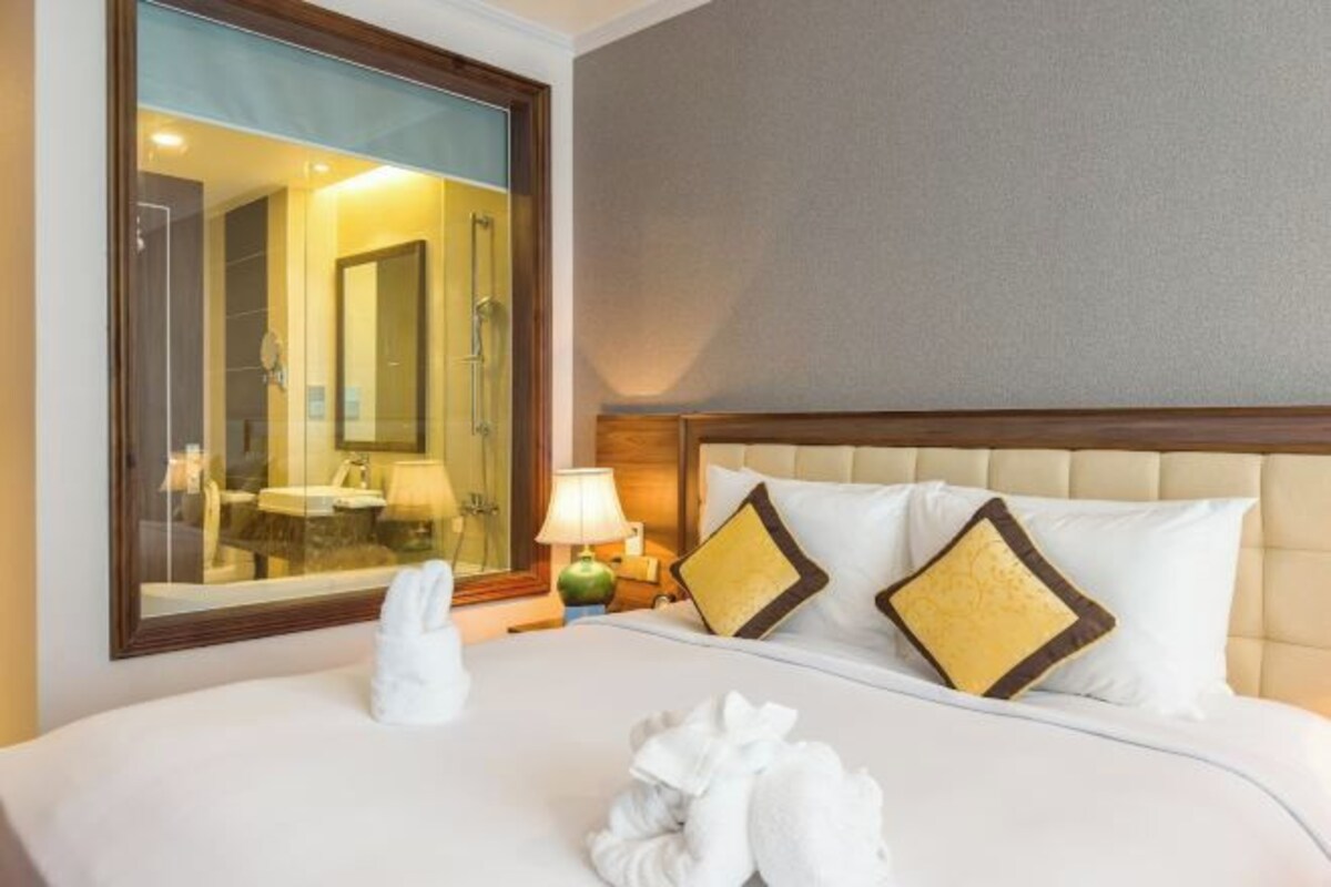Une chambre d’hôtel avec un grand lit, une table de chevet avec une lampe et un miroir qui reflète la salle de bain.