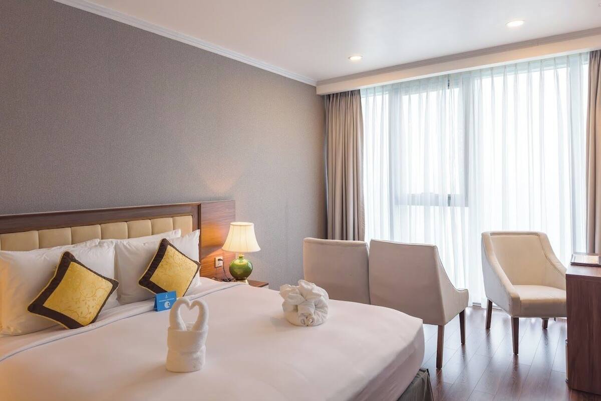 Een hotelkamer met een groot bed, twee stoelen, een bureau en een raam met gordijnen.