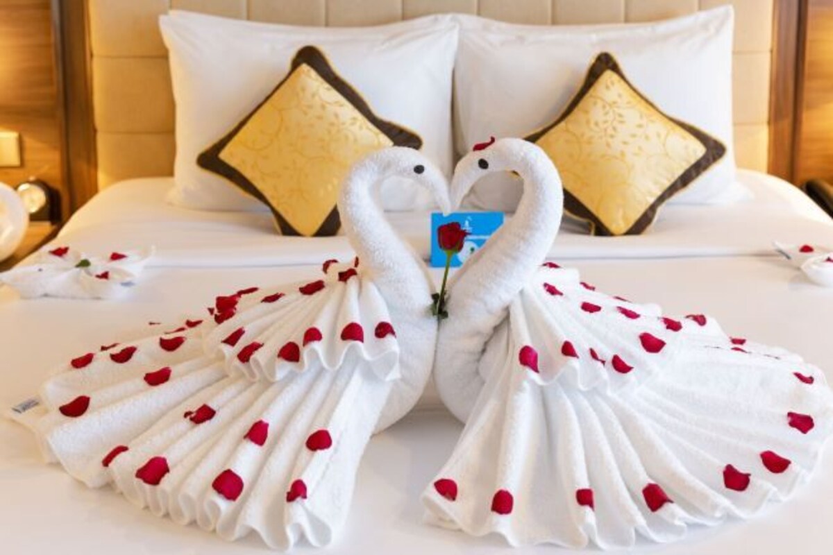 Un lit avec une literie blanche, deux oreillers ornés de motifs dorés et noirs, et une rose posée sur le lit.