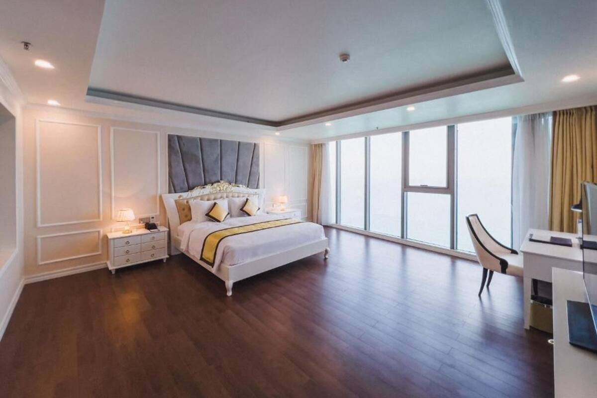 Een ruime slaapkamer met een groot bed, een bureau en een stoel, met een groot raam en uitzicht op de stad.