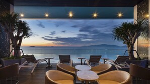 A terrace with lounge chairs and tables, overlooking a body of water and distant mountains. - Nha Trang Horizon Hotel (Bac Nha Trang)