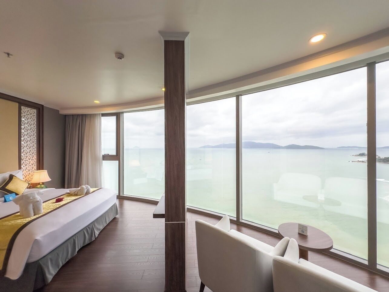 Habitación de hotel con una cama grande, una zona de estar con una mesa y vistas al mar.