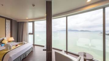 Habitación de hotel con una cama grande, una zona de estar con una mesa y vistas al mar.