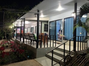 Un bâtiment doté d’un espace extérieur couvert, d’un escalier menant à un balcon et d’un coin repas avec des tables et des chaises.