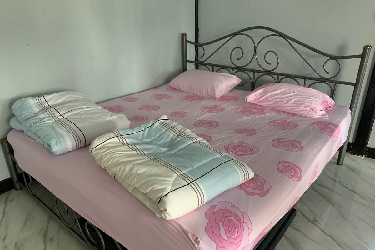 Una cama con estructura metálica, ropa de cama estampada con motivos de rosas rosadas y dos almohadas con diseños a rayas.