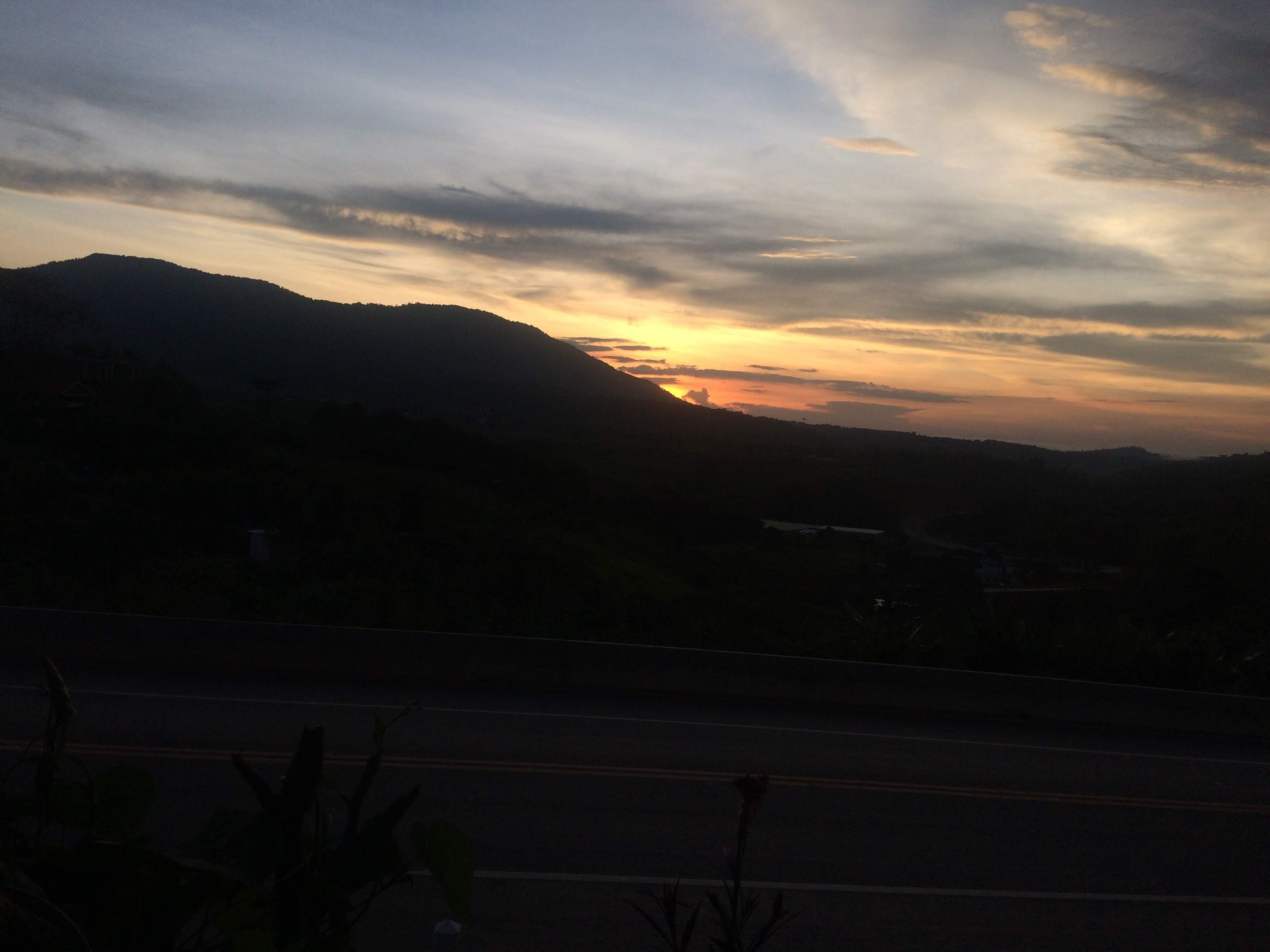 Un coucher de soleil sur un paysage montagneux, avec une route au premier plan.