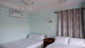Ein Hotelzimmer mit zwei Betten, einem Deckenventilator, einer Klimaanlage, einem Nachttisch und einem Fenster mit Vorhängen.