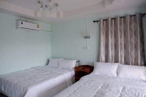 Habitación de hotel con dos camas, ventilador de techo, equipo de aire acondicionado, mesita de noche y ventana con cortinas.