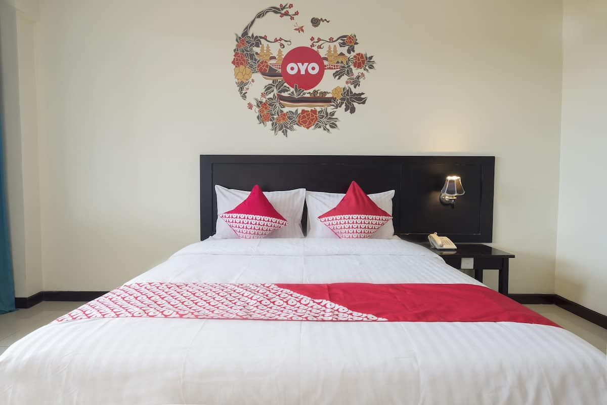 Une chambre d’hôtel avec un lit, des oreillers, une table de chevet, une lampe et un élément décoratif mural.